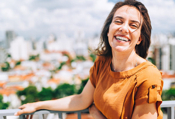 Mulher sorrindo na varanda com a cidade ao fundo